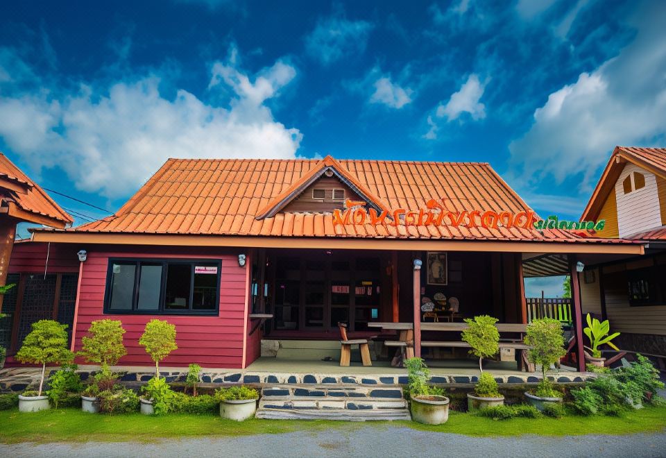 a red wooden house with a red roof , surrounded by green grass and trees , under a blue sky with clouds at Ramiarndao Boutique Place Hotel