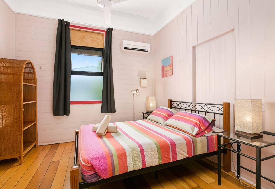 a bedroom with a large bed , wooden floor , and a window covered by black curtains at Dreamtime Travellers Rest