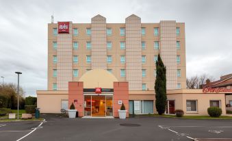 a hotel with a red sign above the entrance , surrounded by trees and cars parked in front at Ibis Clermont-Ferrand Sud Carrefour Herbet