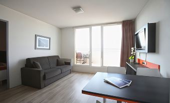 a modern living room with a gray couch , wooden floor , and large windows offering views of the city at Adonis Paris Sud