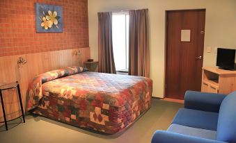 a bedroom with a large bed , blue couch , and wooden walls features a brick - walled door at Catalina Motel Lake Macquarie