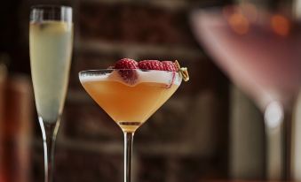 a cocktail with raspberries and a gold stem is being held by a glass of champagne at The Newbridge on Usk