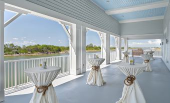 a large room with white tables and chairs , draped in white cloth , is shown with a view of water outside at Beaufort Hotel