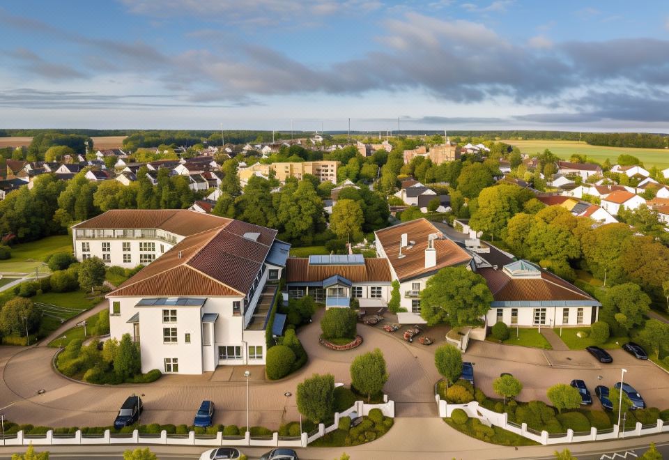 aerial view of a large white building surrounded by trees and a city in the background at Hotel HerzogsPark