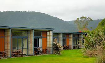 a row of wooden houses with orange and gray exteriors are surrounded by green grass and mountains at Sunset Motel