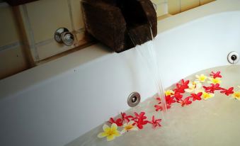 a bathtub filled with water and flowers , with a small waterfall flowing into it at Parn Dhevi Riverside Resort & Spa