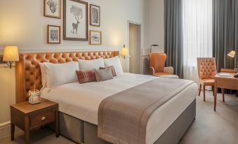 a large bed with a white comforter and orange headboard is in a room with framed pictures on the wall at De Vere Beaumont Estate