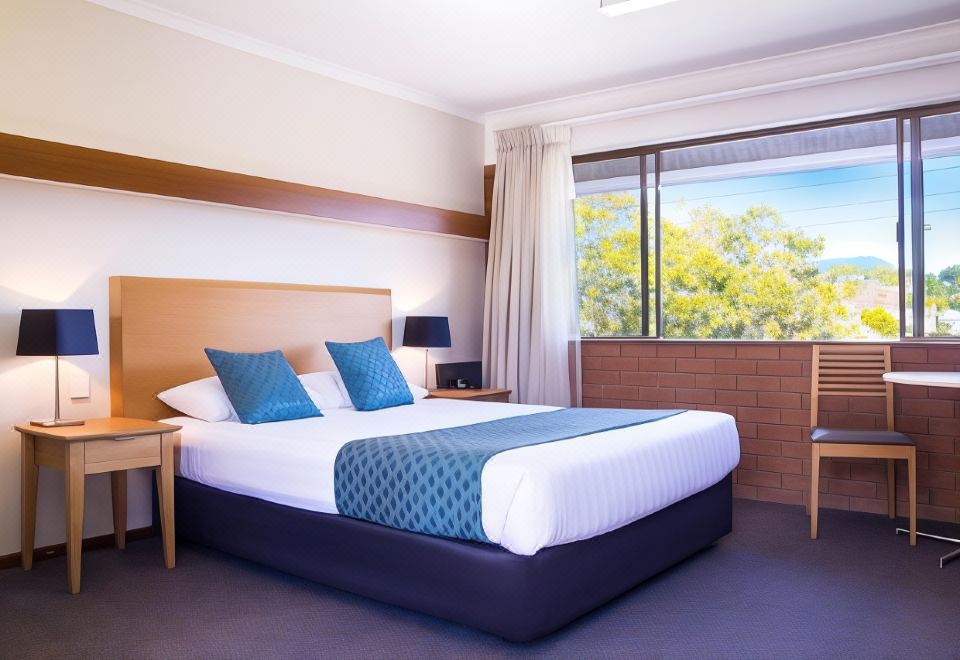 a large bed with a blue blanket and white pillows is in a room with a window at Murwillumbah Motor Inn