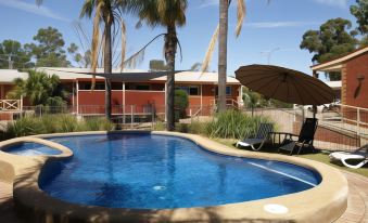 a large swimming pool with a beach umbrella and lounge chairs in front of a house at Echuca Motel