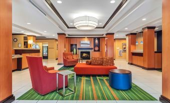 a modern hotel lobby with an orange couch , red chairs , and a fireplace under a ceiling light at Fairfield Inn & Suites Worcester Auburn