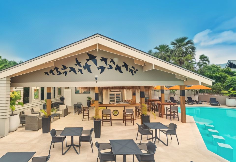 an outdoor patio area with tables , chairs , and a bar , surrounded by palm trees and a swimming pool at Sunset Resort