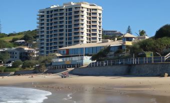 a tall building is situated next to a beach , with a pier extending into the water at Coolum Caprice