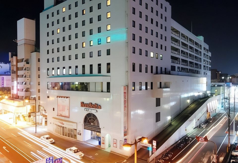 a city street at night , with a large white building on the left side of the road and multiple cars on the road at Airline Hotel