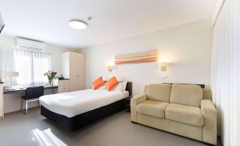 a modern hotel room with a bed , couch , and desk , along with a window and light fixtures at Ibis Styles Canberra Tall Trees