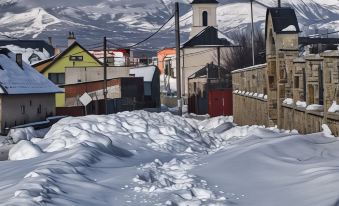 a snowy street in a small town with buildings and mountains in the background , under a clear blue sky at VeLa