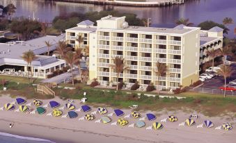 a large white building with balconies and palm trees is surrounded by colorful umbrellas on the beach at Delray Sands Resort