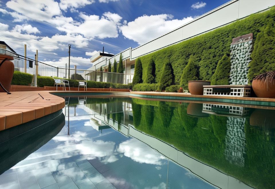 a large pool is surrounded by a green hedge and has a white building in the background at Admiralty Inn
