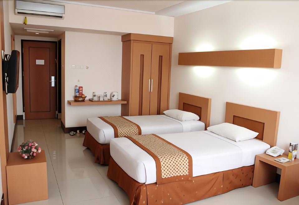 a hotel room with two beds , each made up with white sheets and brown bedspreads , next to a wooden wardrobe at Ceria Hotel Jambi by Tritama Hospitality