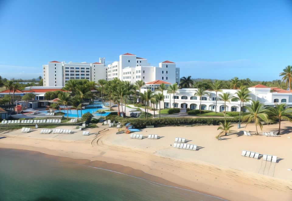 a beachfront resort with white buildings , palm trees , and a swimming pool under a clear blue sky at Aquarius Vacation Club at Dorado del Mar