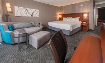 a modern hotel room with a large bed , couch , and table , along with some personal belongings on the desk at Courtyard by Marriott Fairfax Fair Oaks