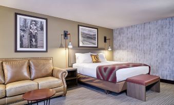 a modern hotel room with a large bed , two nightstands , and a couch , along with framed art on the walls at Yellowstone Park Hotel