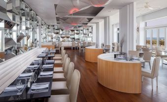 a modern restaurant with wooden tables and chairs , white chairs , and a large circular counter at Allegria Hotel