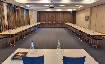 a large conference room with a long table and chairs , water bottles on the table , and a projector screen at B&B Hotel Affi - Lago di Garda
