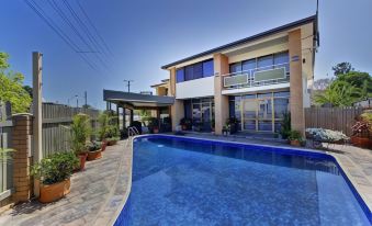 a modern , two - story house with a large swimming pool in the backyard , surrounded by potted plants and an outdoor seating area at Raintree Motel