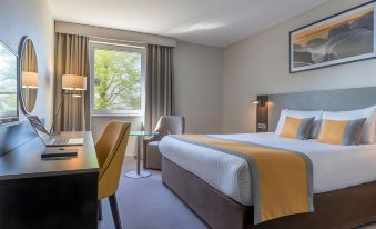 a modern hotel room with a large bed , two nightstands , and a window offering a view of trees at Maldron Hotel Belfast International Airport