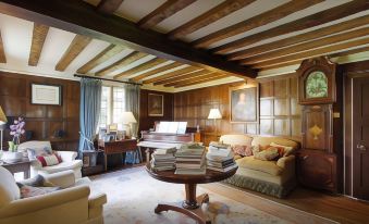 a cozy living room with wooden furniture , including a piano , couch , and coffee table , surrounded by books on the floor at B&B Harlington Manor