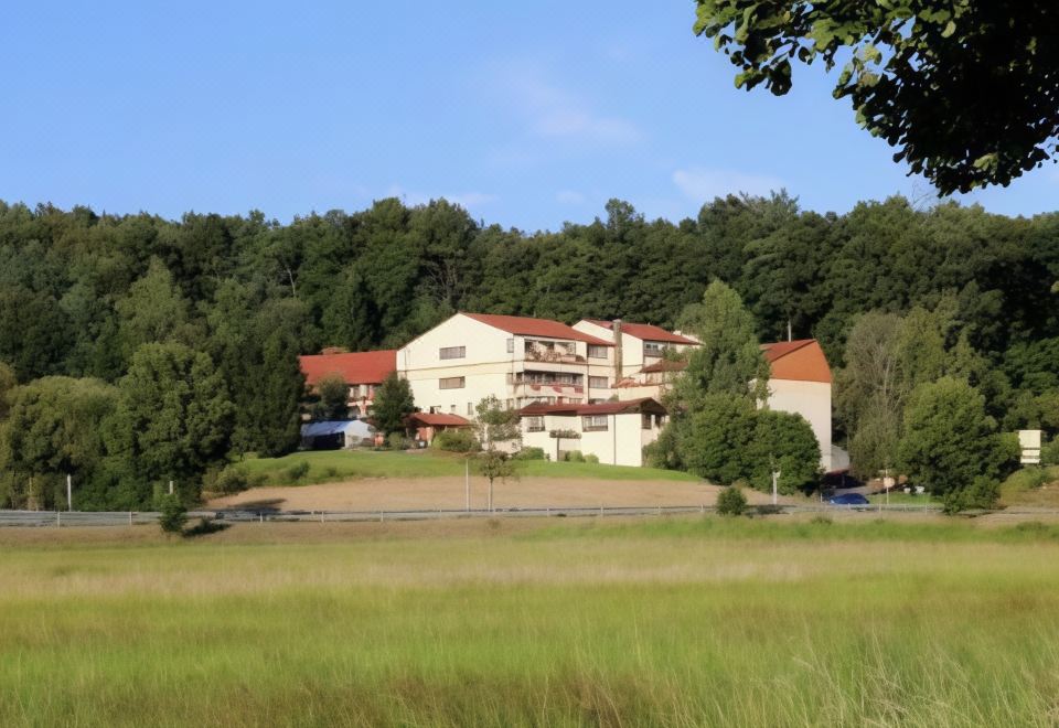 a large building with a red roof is surrounded by trees and grass in a field at Hotel Sonnenblick