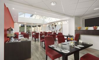 a dining room with red chairs and tables , white tablecloths , and a large window with a skylight at Days Inn by Wyndham London Stansted Airport