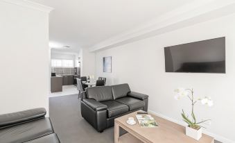 a modern living room with a black leather couch , wooden coffee table , and television mounted on the wall at East Maitland Executive Apartments