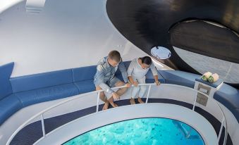 a man and a woman are sitting on a blue couch in a room with a large round bathtub filled with blue water at Niva Kurumba Maldives