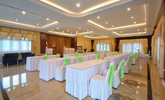a large banquet hall with multiple tables set up for a formal event , each table covered in white tablecloths and adorned with green bows at Princess River Kwai Hotel