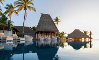 a large swimming pool surrounded by palm trees , with several lounge chairs and umbrellas placed around the pool at Matamanoa Island Resort