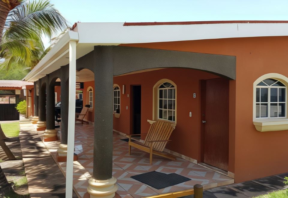 a porch with a wooden chair and a red table , situated in front of a building with a blue roof at Hotel Miraflores