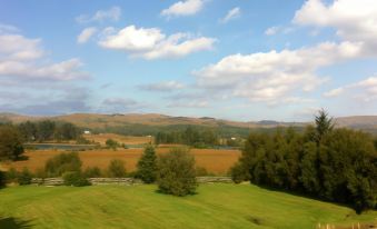 a serene rural landscape with rolling hills , grassy fields , and trees under a blue sky dotted with clouds at Loch Shiel Hotel