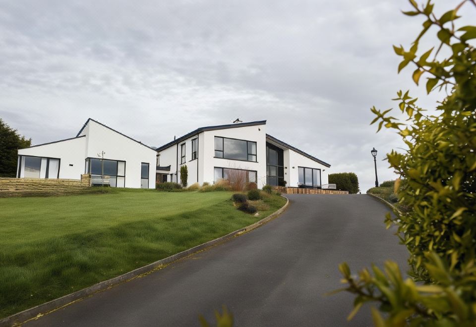 a modern , white house with black trim and large windows , situated on a grassy hill overlooking a road at Peartree Hill