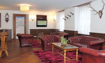 a cozy living room with red leather couches and chairs , a coffee table , and a television at Hotel Weisses Kreuz