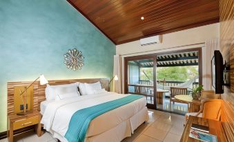 a large bed with white linens and a blue blanket is in a room with wooden walls , an open door leading to an outdoor balcony at Tivoli Ecoresort Praia do Forte