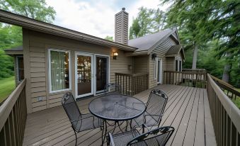 a wooden deck with a table and chairs , surrounded by trees and a house in the background at Telemark Northwoods Lodging