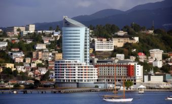 a tall building is situated on a waterfront , with a sailboat in the background and mountains in the background at Simon Hotel