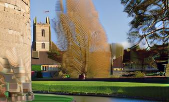 a brick building with a golden tree in front of it , surrounded by grass and a body of water at The George at Nunney
