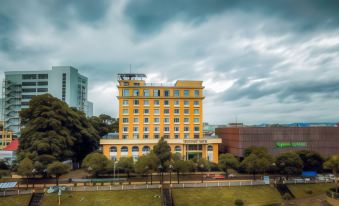 a tall yellow building surrounded by trees , with a cloudy sky in the background at Indochine Hotel