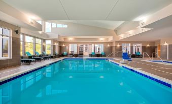 an indoor swimming pool with a large window , surrounded by lounge chairs and umbrellas , in a well - lit room at Residence Inn Kingston
