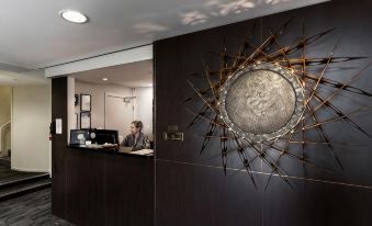 a woman is sitting at a desk in a room with a reception desk and a large circular wall art at St Ives Apartments