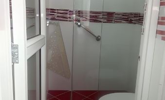 a white toilet is in a bathroom with red and white tile flooring , a shower stall , and a glass door at Montesion