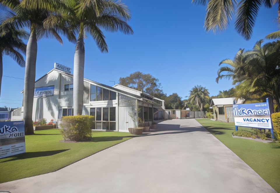 a white building with palm trees and a driveway is situated in front of it at Iluka Motel