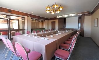 a conference room with a long table , pink chairs , and white plates set for a meeting at Hotel Imperial